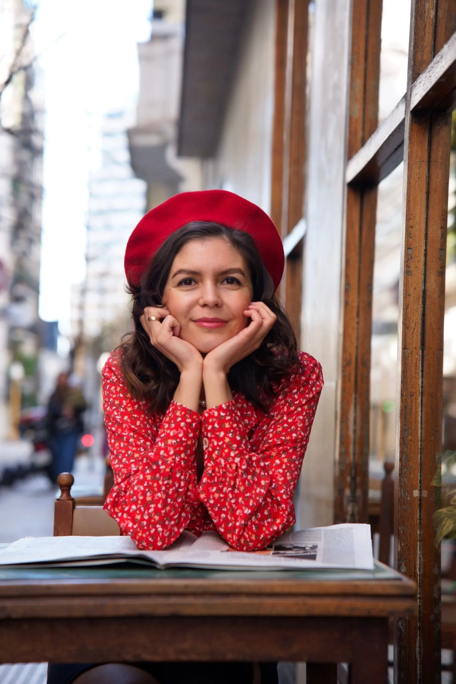 Elvina apoyada en una mesa de café en Buenos Aires, con boina roja y camisa floreada